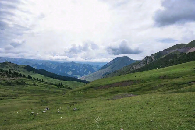 Green hills frame an open valley, with distant mountains beneath a wide cloudy sky.