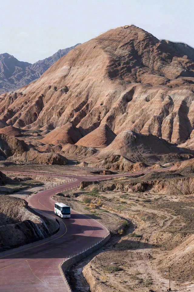 A curved road passes through steep brown rock formations, with a vehicle on the bend.