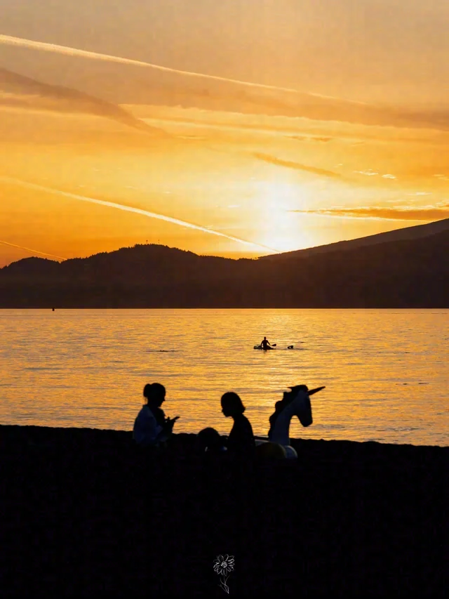Seated silhouettes face a golden sunset over the water, with a small craft in the distance.