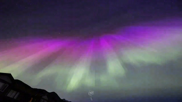 Green and purple bands of light spread across the night sky above dark roof silhouettes.