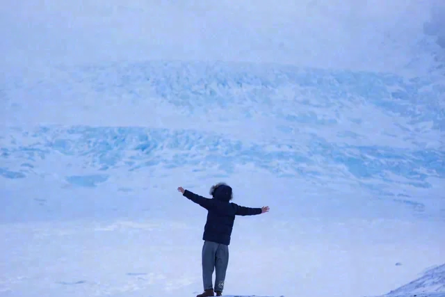 A person stands with both arms extended in a wide blue-toned snowy landscape.
